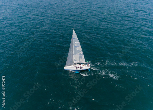 Aerial view a lonely isolated sailboat under the sail with tall mast going in still sea 
