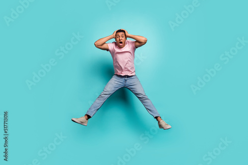 Full length photo of pretty impressed man dressed pink t-shirt jumping high arms hands head isolated turquoise color background