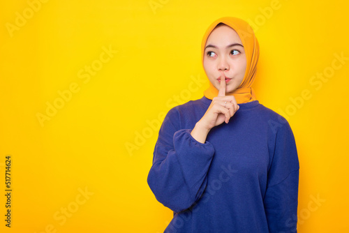 Fotografie Serious young Asian Muslim woman dressed in casual sweater showing shh gesture,