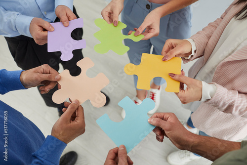 Group of people joining jigsaw puzzle parts. Creative business team come up with different ideas while trying to find solution of difficult problem. Cropped close up shot. Teamwork, innovation concept