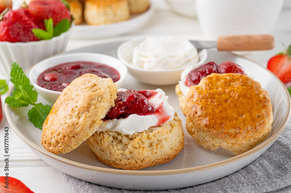 Homemade British Scones with cream cheese, strawberry jam and a cup of tea on a white wooden background. Homemade British Scones with cream cheese, strawberry jam and a cup of tea on a white wooden background.