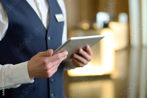 Fotografiet Digital tablet in hands of young male receptionist of luxurious modern hotel sta
