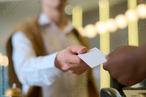 Hand of young male travler or guest of hotel taking keycard held by African American female receptionist after registration photo