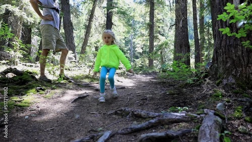 Cute little blond girl running in the forest on the hiking trails and father waiting for her in  slow motion.