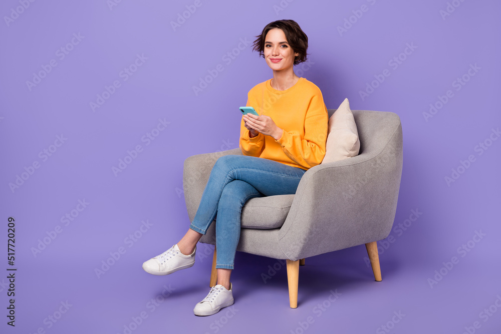 Full size portrait of positive nice person sit chair hold use telephone gadget isolated on purple color background Full size portrait of positive nice person sit chair hold use telephone gadget isolated on purple color background