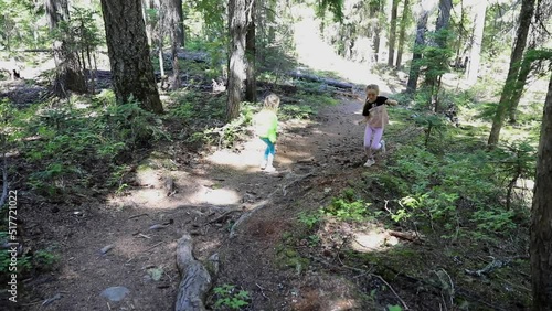 Two little girls are running in the forest on the hiking trails during family trip with children.