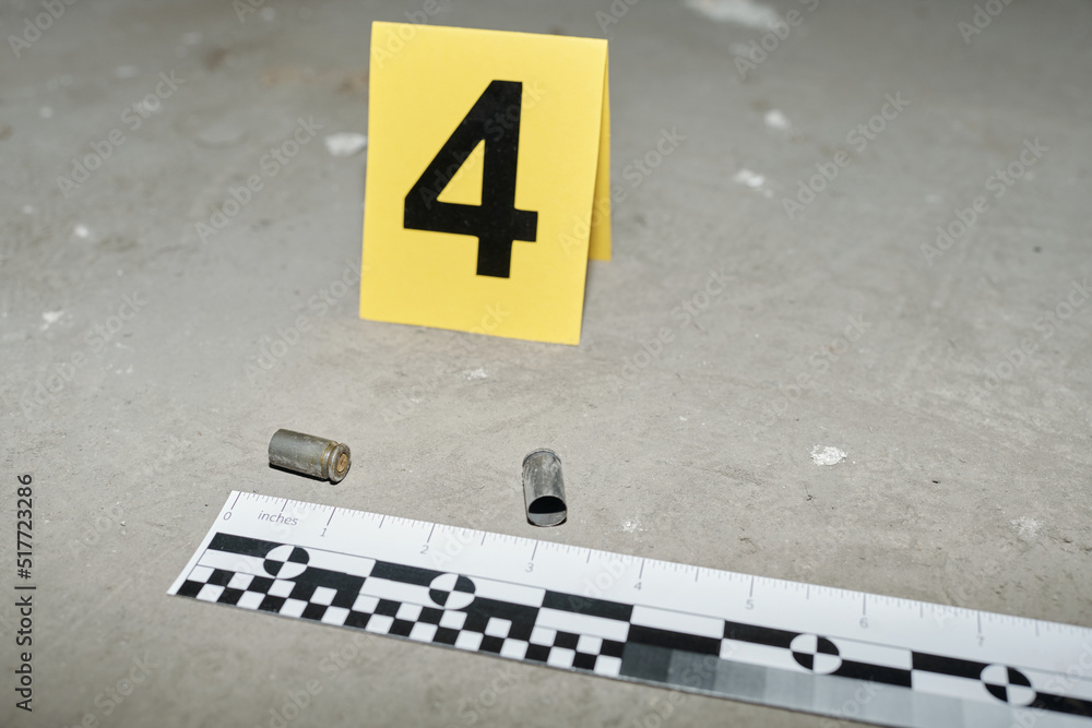 Fototapeta premium Yellow card with number four standing on asphalt by two empty cartridge cases left on crime scene shot from handgun of murderer