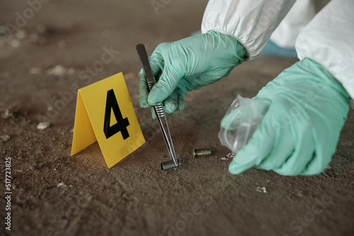 Hands of criminological expert holding empty cartridge case with metal pincers while putting it into plastic packet while seeking for evidences photo