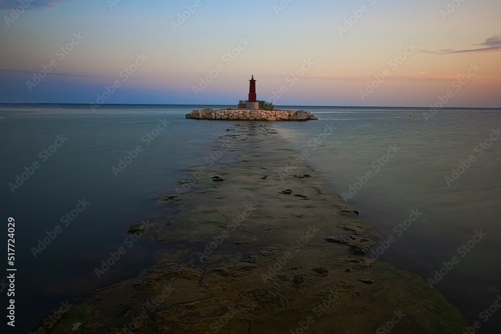 Breakwater with lighthouse in the port of Villajoyosa, Alicante, Spain, at sunset time, with calm waters and blue and orange cloudless sky Breakwater with lighthouse in the port of Villajoyosa, Alicante, Spain, at sunset time, with calm waters and blue and orange cloudless sky