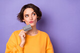 Portrait of attractive minded curious girl holding in bank card deciding copy space isolated over violet lilac color background