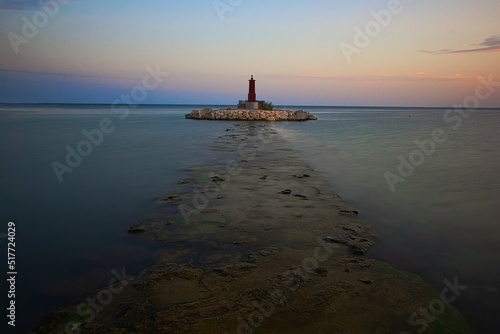 Breakwater with lighthouse in the port of Villajoyosa, Alicante, Spain, at sunset time, with calm waters and blue and orange cloudless sky