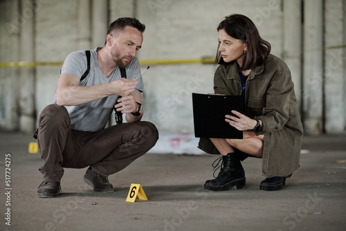 Detective inspector or policeman showing empty cartridge case to criminological expert making notes in document photo