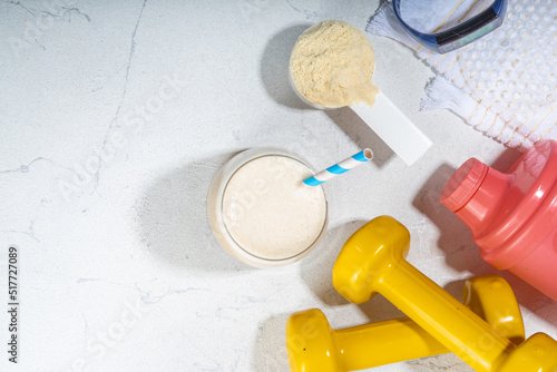 Vanilla white protein shake glass, with straw, with protein powder, dumbbell, towel and fitness accessories, on white sport bar table background copy space