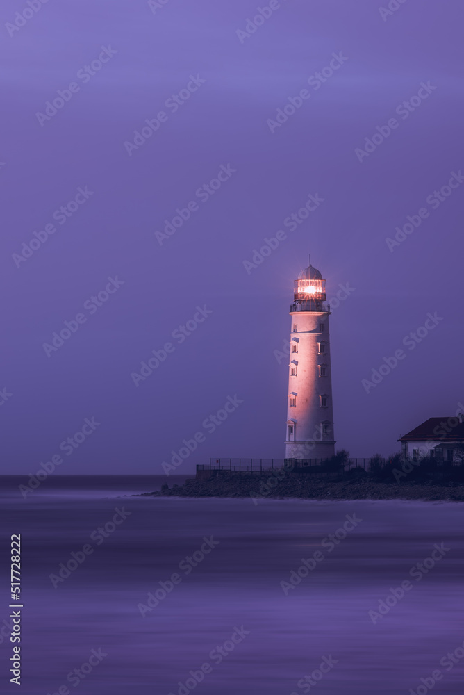 A lighthouse on the coast of the sea at dusk, its bright lamp is a landmark for ships. Seascape, nature background.