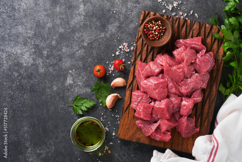 Raw chopped beef meat. Raw organic meat beef or lamb, spices, herbs on old wooden board on dark grey concrete background. Goulash. Raw uncooked meat. Meat with blood. Top view with copy space.