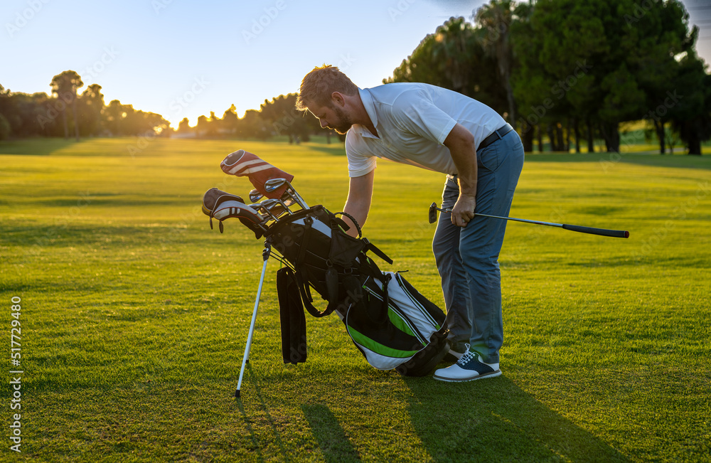 Fototapeta premium Young handsome man at the course holding something in the golf bag.