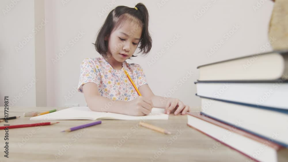 Adorable asian girl is doing her homework on the table with a lot of books and pencil. It shows concept of smart and clever child learning by herself to gain knowledge which is basic education. Adorable asian girl is doing her homework on the table with a lot of books and pencil. It shows concept of smart and clever child learning by herself to gain knowledge which is basic education.