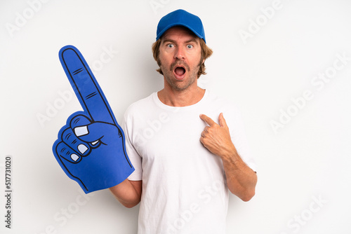 adult blond man looking shocked and surprised with mouth wide open, pointing to self. number one hand fan concept photo