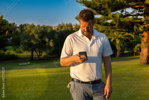 Portrait of young handsome golf player at golf club using smartphone.