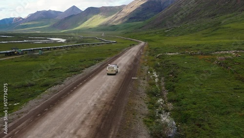 Road trip through Alaska wild mountains - van driving on dirt soil road at the base of Brooks mountains Range near Trans Alaska crude oil Pipeline - aerial following  photo