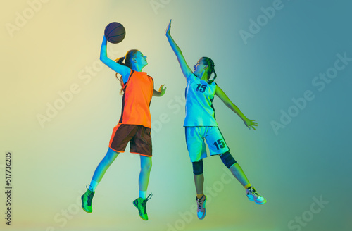 Attack and defense. Female basketball players, young girls, teen in action with basketball ball isolated on neoned background. Concept of sport, team, enegry, competition, skills