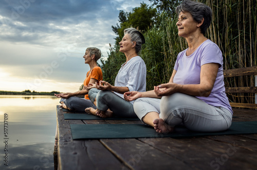 Group of senior woman doing yoga exercises by the lake.