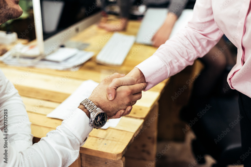 Unrecognizable coworkers shaking hands in office Unrecognizable coworkers shaking hands in office