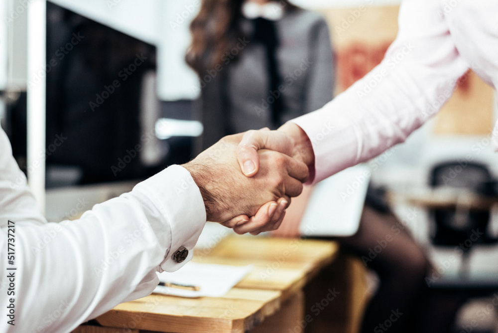 Unrecognizable coworkers shaking hands in office Unrecognizable coworkers shaking hands in office