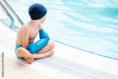 Adorable kid in shorts sitting at poolside and looking away