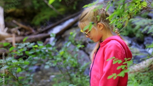 Beautiful child girl on a hike near waterfall and wild blueberries bush