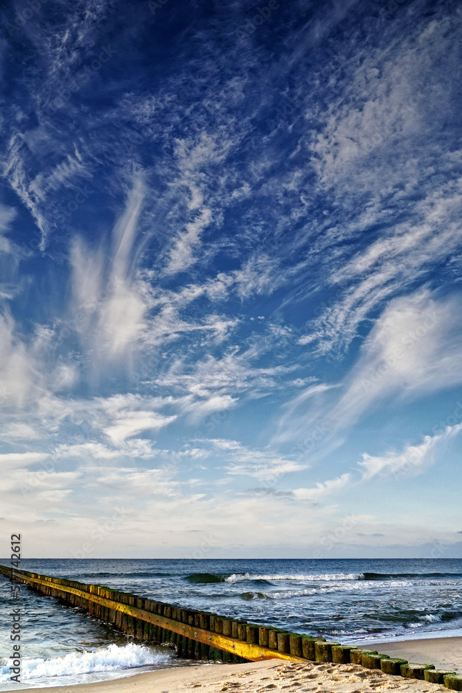 Sea sand shore, breakwater and phenomenal clouds in the blue sky