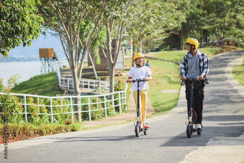 Sibling on vacation having fun to ride electric scooter through the street park. Youth Leisure Family Concept.