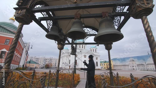 Orthodox monk rings large church bells in belfry at ancient christian monastery on gloomy day. Religion service photo