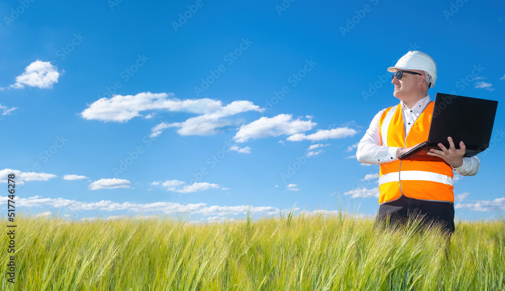 builder holds a laptop. An engineer against the backdrop of the blue sky.  engineer-builder plans in the future construction in the clean field. A man examines a place where he plans to start building