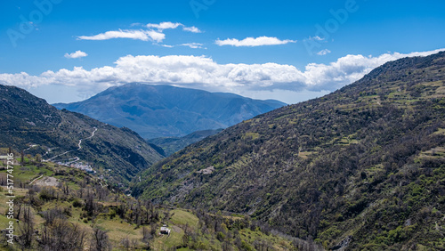 Impressive view from the top on picturesque mountain valley with trees and bushes in sunny summer day with blue sky and white clouds in background.