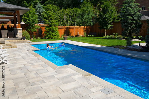 Mother and daughter swimming in new back yard pool with  patio of pavers and green lawn and gardens © Reimar