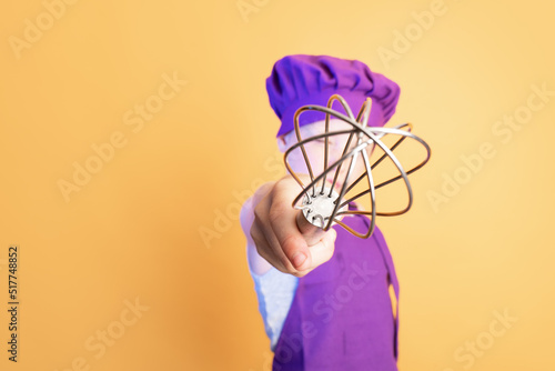 Little baker showing mixer whisk against yellow background
