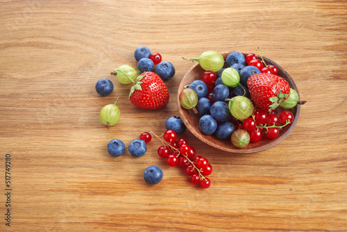 Berries mix in in a heart shaped bowl spilled on rustic wooden table