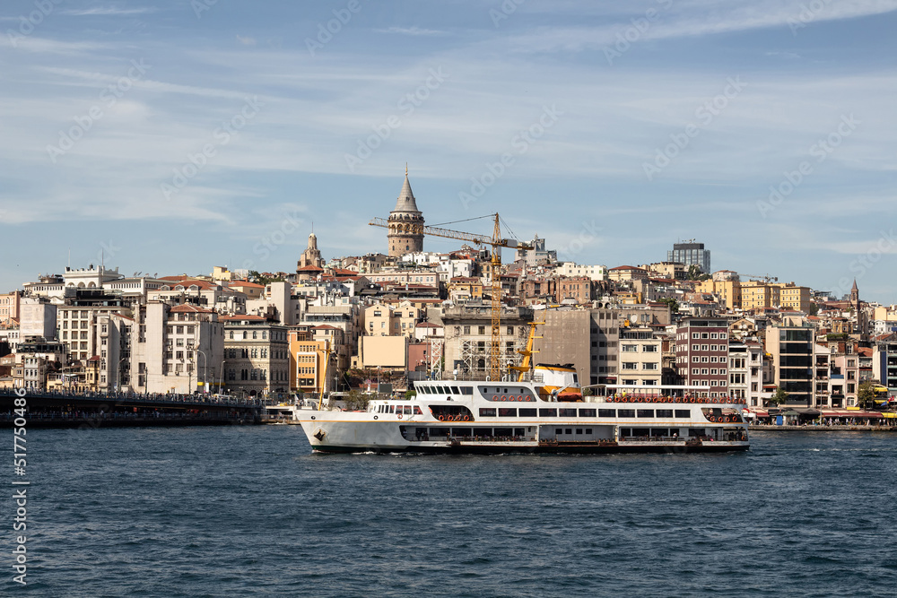 View of a traditional ferry boat on Golden Horn part of Bosphorus in Istanbul. Galata tower and Beyoglu district are in the view. It is a sunny summer day.