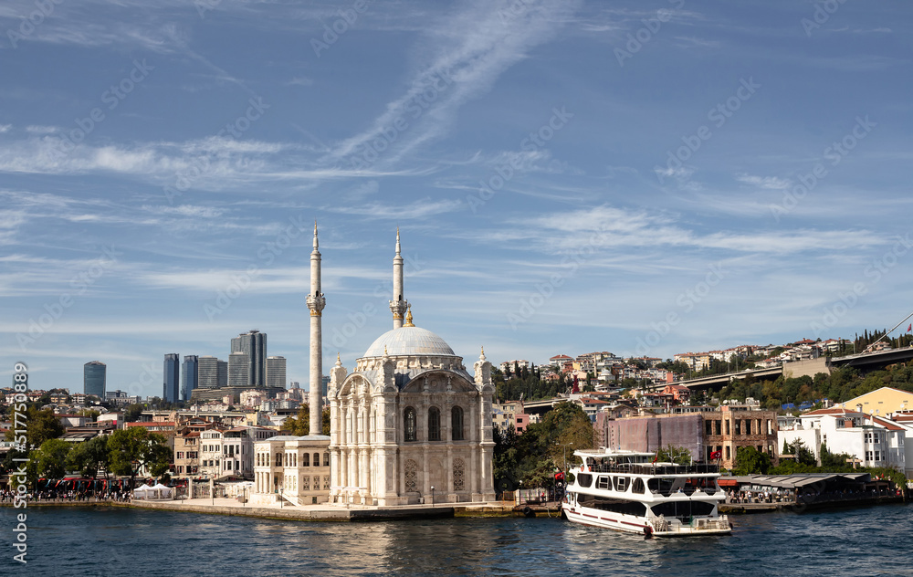 View of a moored cruise tour boat on Bosphorus, historical Ortakoy mosque in Istanbul. It is a sunny summer day. Beautiful travel scene.