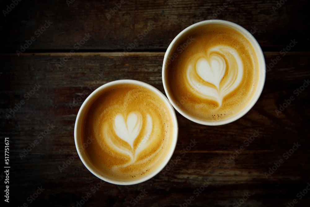 Two cups of cappuccino with a heart latte art. Vintage wooden background, top view. Two cups of cappuccino with a heart latte art. Vintage wooden background, top view.