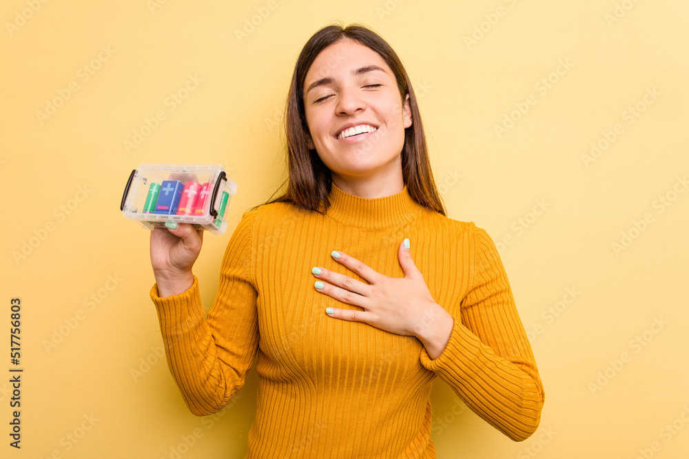Young caucasian woman holding a batteries box isolated on yellow background laughs out loudly keeping hand on chest. Young caucasian woman holding a batteries box isolated on yellow background laughs out loudly keeping hand on chest.