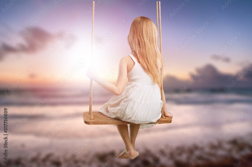 Child tourist swinging on swing, sandy beach. Tropical vacation.