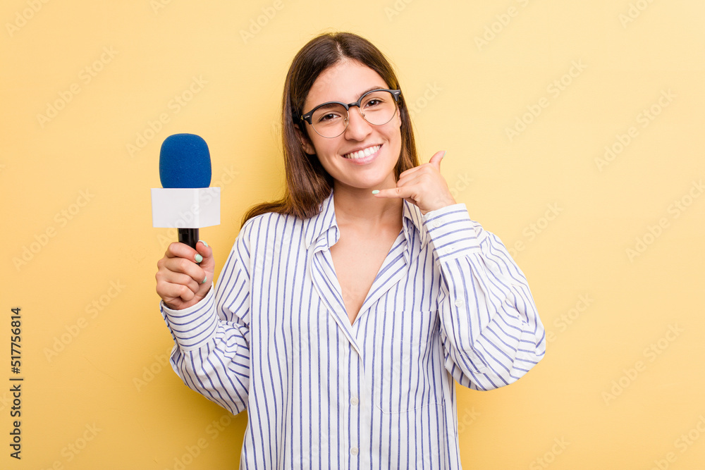 Young caucasian presenter TV woman isolated on yellow background showing a mobile phone call gesture with fingers. Young caucasian presenter TV woman isolated on yellow background showing a mobile phone call gesture with fingers.