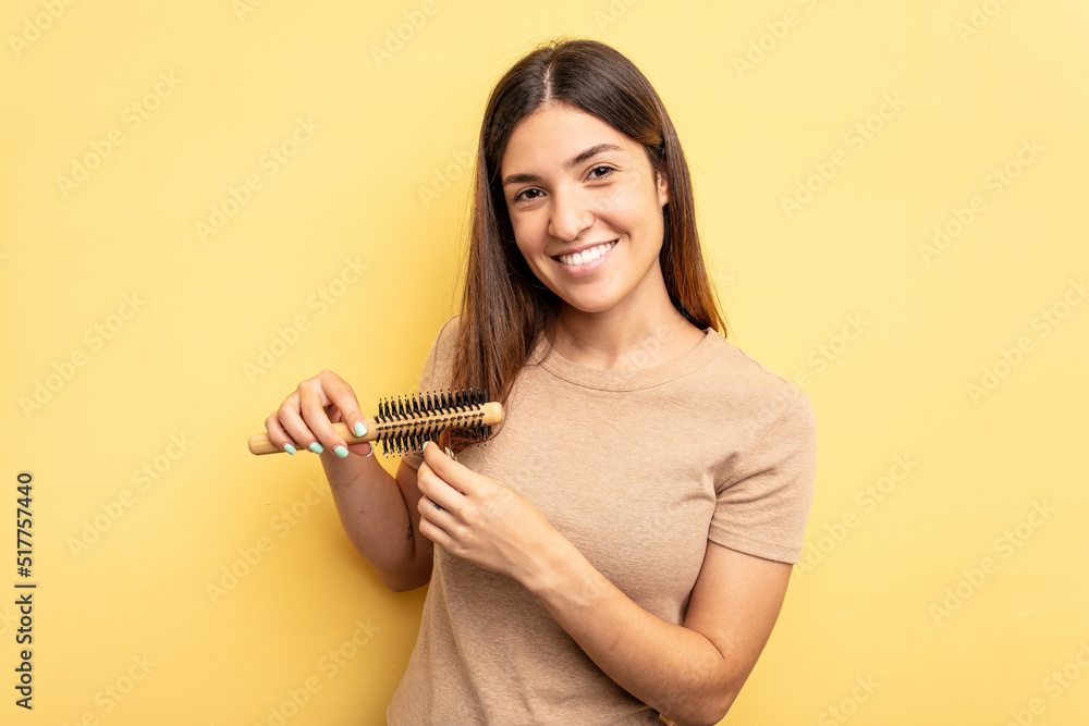 Young caucasian woman holding a brush hair isolated on yellow background Young caucasian woman holding a brush hair isolated on yellow background