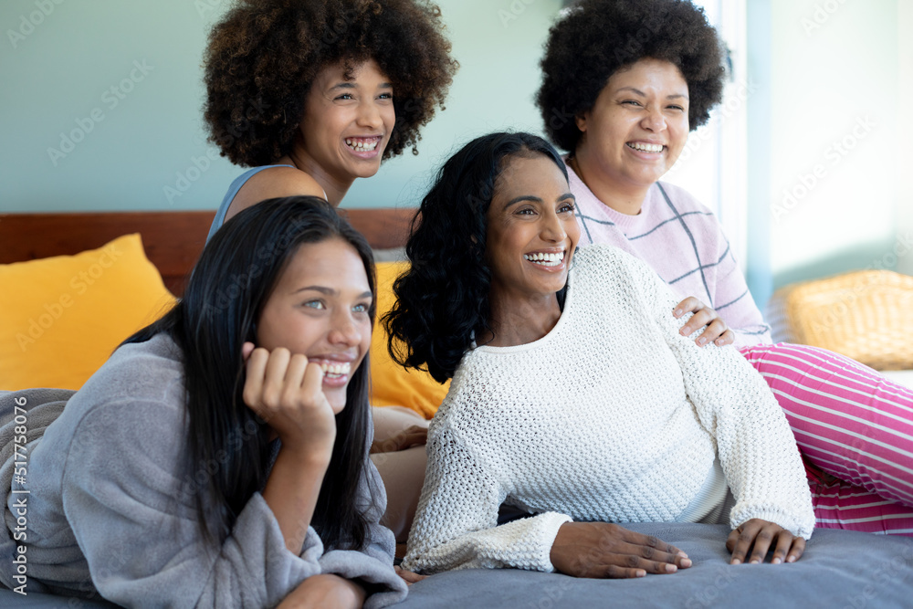 Cheerful biracial young female friends looking away while spending leisure time together on bed Cheerful biracial young female friends looking away while spending leisure time together on bed