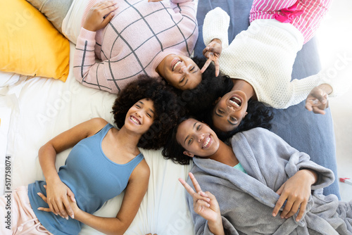 High angle portrait of happy biracial young female friends lying and relaxing on bed at home