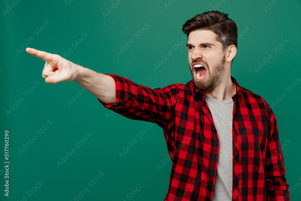 Young sad furious angry man he 20s wearing red shirt grey t-shirt point index finger aside scream shout command do it isolated on plain dark green background studio portrait People lifestyle concept. Young sad furious angry man he 20s wearing red shirt grey t-shirt point index finger aside scream shout command do it isolated on plain dark green background studio portrait People lifestyle concept.