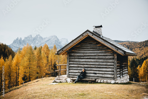 Incredible autumn view at Valfreda valley in Italian Dolomite Alps. Wooden cabin, yellow grass, orange larches forest and snowy mountains peaks on background. Dolomites, Italy. Landscape photography photo