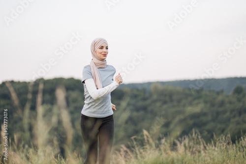 Healthy sport woman in hijab in active clothes enjoying morning run at green park. Muslim woman in hijab spending leisure time for training on fresh air.